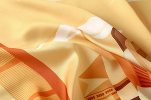 Close-up of ginger yellow satin silk scarf showing smooth texture and geometric patterns