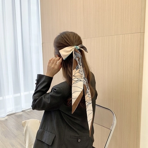 Close-up of floral silk skinny scarf tied as a bow hair accessory on a woman back view