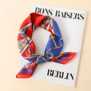 Macro detail of luxury satin scarf with equestrian belt and chain prints on a magazine
