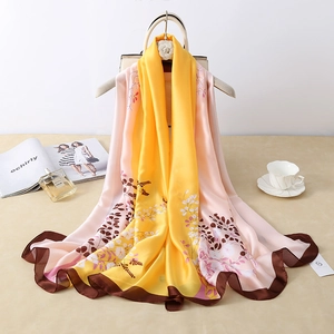 Elegant floral silk scarf with yellow pink gradient hanging on a stylish beige bag