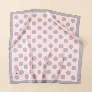 Flat lay of pink satin square scarf with grey polka dots and red butterfly detail
