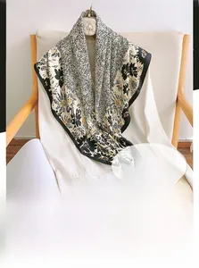 Detailed view of a 90cm floral silk-feel scarf draped on a white shirt and wooden chair
