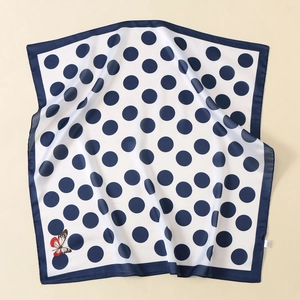 Detailed close-up of a satin silk scarf with navy polka dots and a colorful butterfly motif