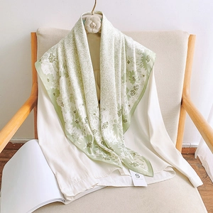 Detail of floral print silk scarf in soft green draped elegantly on a white shirt