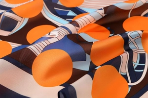 Close-up detail of smooth satin scarf fabric with orange polka dots and geometric patterns