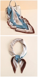 Dettaglio di un foulard in raso a blocchi di colore legato al manico di una borsa beige
