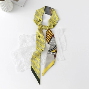 Close-up of a floral yellow twilly silk scarf tied in a bow with chain and R letter patterns