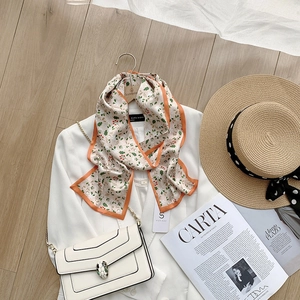 Detail of floral silk scarf with orange edges styled on a white blazer and accessories
