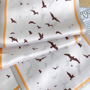 Detailed view of ink-style bird print silk scarf with vibrant orange striped edging