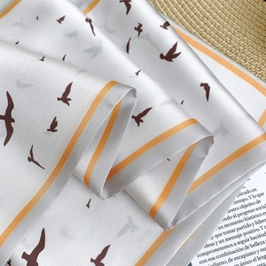Detail of silk scarf with orange borders and flying bird print on a magazine backdrop