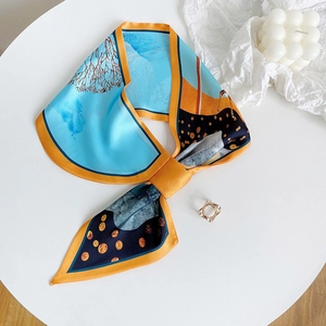 Dettaglio del foulard in seta azzurro e arancione annodato a fiocco su un espositore bianco