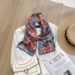 Detail of silk-like blue and orange floral scarf styled with a white blazer and snake chain bag