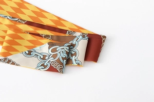 Detailed close-up of silk-like ribbon scarf with orange diamond and chain print