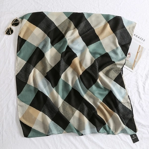 Detail shot of a geometric plaid silk scarf with brand tag on a soft fabric background