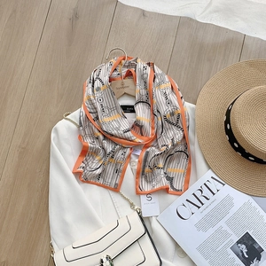 Chic long silk scarf with chain print and orange border styled on a white blazer