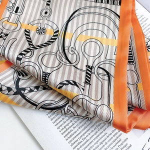Close-up of elegant equestrian silk scarf featuring orange borders and horse bit patterns