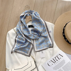 Elegante blauwe satijnen sjaal met gouden gesp-prints op een witte blazer en tas
