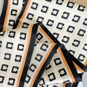 Détail d'un foulard en satin rayé avec imprimé C et bordures orange contrastées