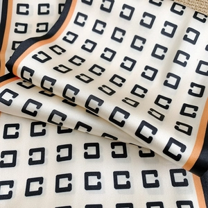 Détail d'un élégant foulard en satin crème avec imprimé C et bordures noir-orange