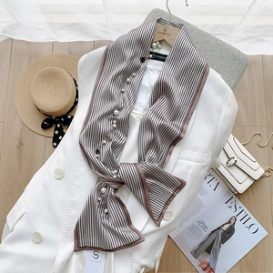 Détail d'un foulard en satin rayé avec pendentif perle sur un blazer blanc chic