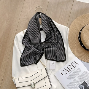 Détail d'un foulard en satin à rayures noires et blanches avec un blazer blanc chic
