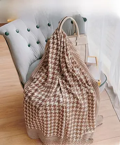 Brown and cream houndstooth scarf draped on a sofa next to a beige handbag
