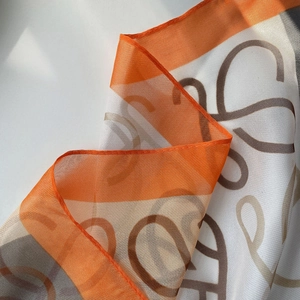 Close-up detail of lightweight beach scarf with orange edges and abstract dot print