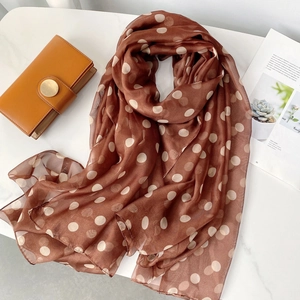 Flat lay of brown polka dot beach scarf on marble surface with luxury accessories