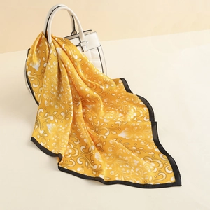 Close-up of yellow silk scarf with white vintage patterns draped over a white leather bag