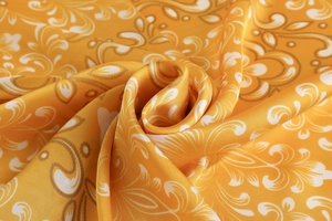 Detailed close-up showing the golden paisley pattern and silky texture of the square scarf