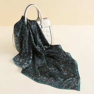 Close-up of silk-like square scarf featuring teal paisley patterns and gold-toned borders