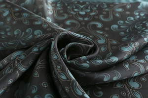 Detail of silk satin fabric showing teal baroque paisley patterns and glossy texture
