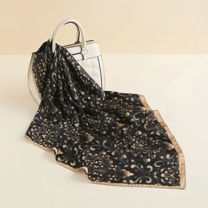 Detailed macro view of black and gold paisley silk scarf draped on a white handbag