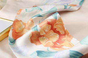 Detail of silk scarf showing orange floral patterns and satin texture on pink background