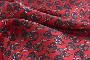 Close-up of red silk scarf with golden chain patterns and vintage equestrian letter motifs
