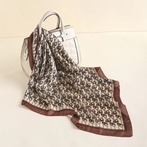 Detail of elegant paisley silk scarf with chain pattern draped over a white luxury handbag