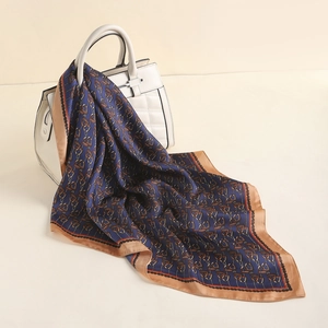 Close-up of silk scarf with navy paisley pattern and golden border on white handbag