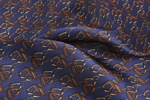 Detail macro view of silk scarf fabric showing twill weave and orange stirrup pattern