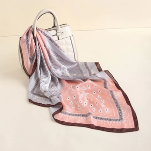 Detail of paisley silk-like scarf with gold trim draped on a white quilted handbag