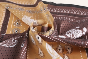 Close-up of silk square scarf featuring gold paisley patterns and premium satin texture