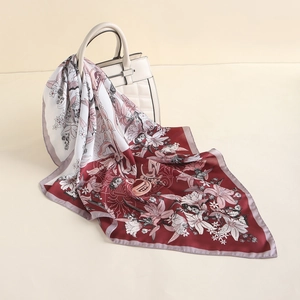 Detail of floral silk scarf with lily and butterfly prints draped on a quilted bag