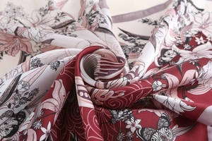 Detail of burgundy satin silk scarf featuring butterfly and lily patterns with a golden border