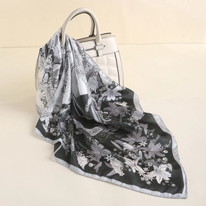 Close-up of elegant silk-like square scarf with lily flowers draped on a luxury white handbag