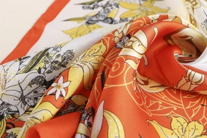 Macro view of retro floral silk scarf with golden edges and elegant orange botanical prints