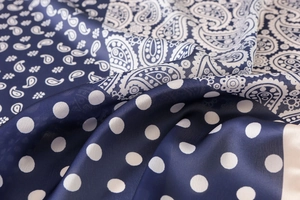 Dettaglio macro del tessuto satinato setoso con motivi paisley e trame a pois chic