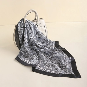 Detail of silk-like paisley square scarf with gold border draped on a white handbag