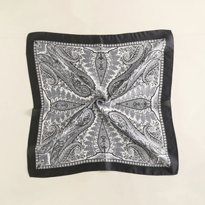 Detail shot of square silk scarf featuring grey paisley patterns and elegant black borders
