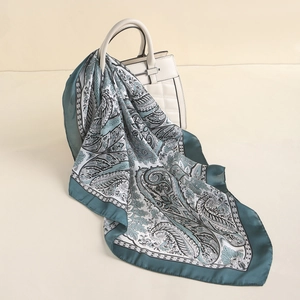 Detail of dark green paisley silk scarf draped over a beige handbag in close-up shot