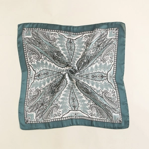 Detailed macro view of paisley silk-feel square scarf with gold trim and emerald green borders