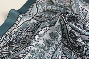 Detail of green paisley silk-like scarf featuring golden edges and fine rolled hems